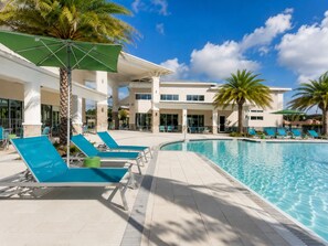 Un espace piscine doté de chaises longues, de palmiers et d’un bâtiment avec de grandes fenêtres.
