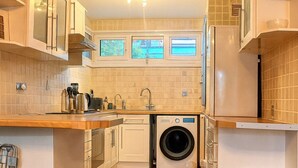 Una cucina compatta con lavatrice, piano di lavoro in legno e mobili bianchi.