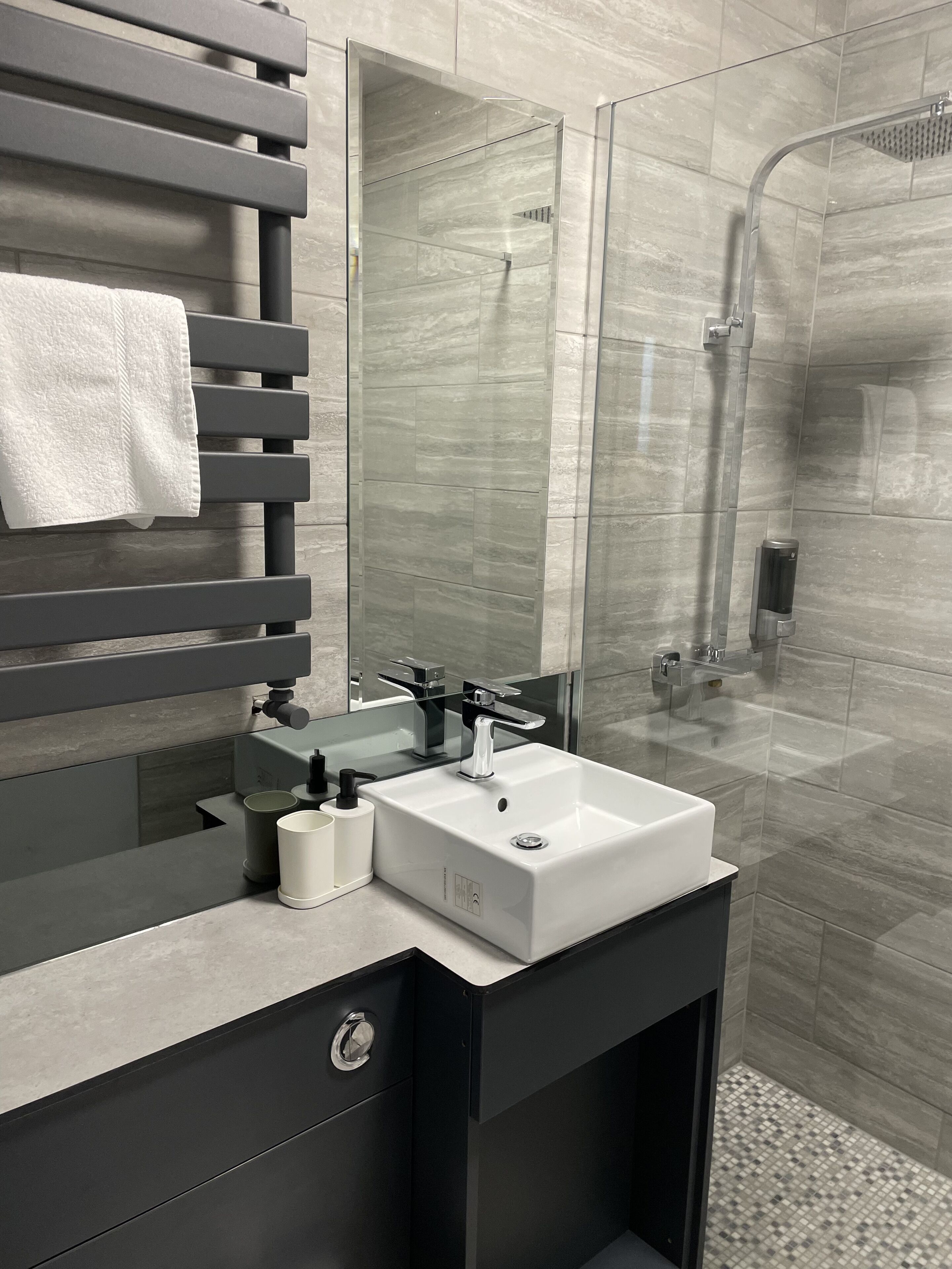 A modern bathroom with a large mirror, a white sink, and a glass-enclosed shower.
