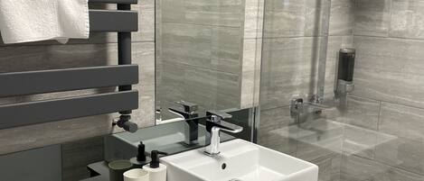 A modern bathroom with a large mirror, a white sink, and a glass-enclosed shower.