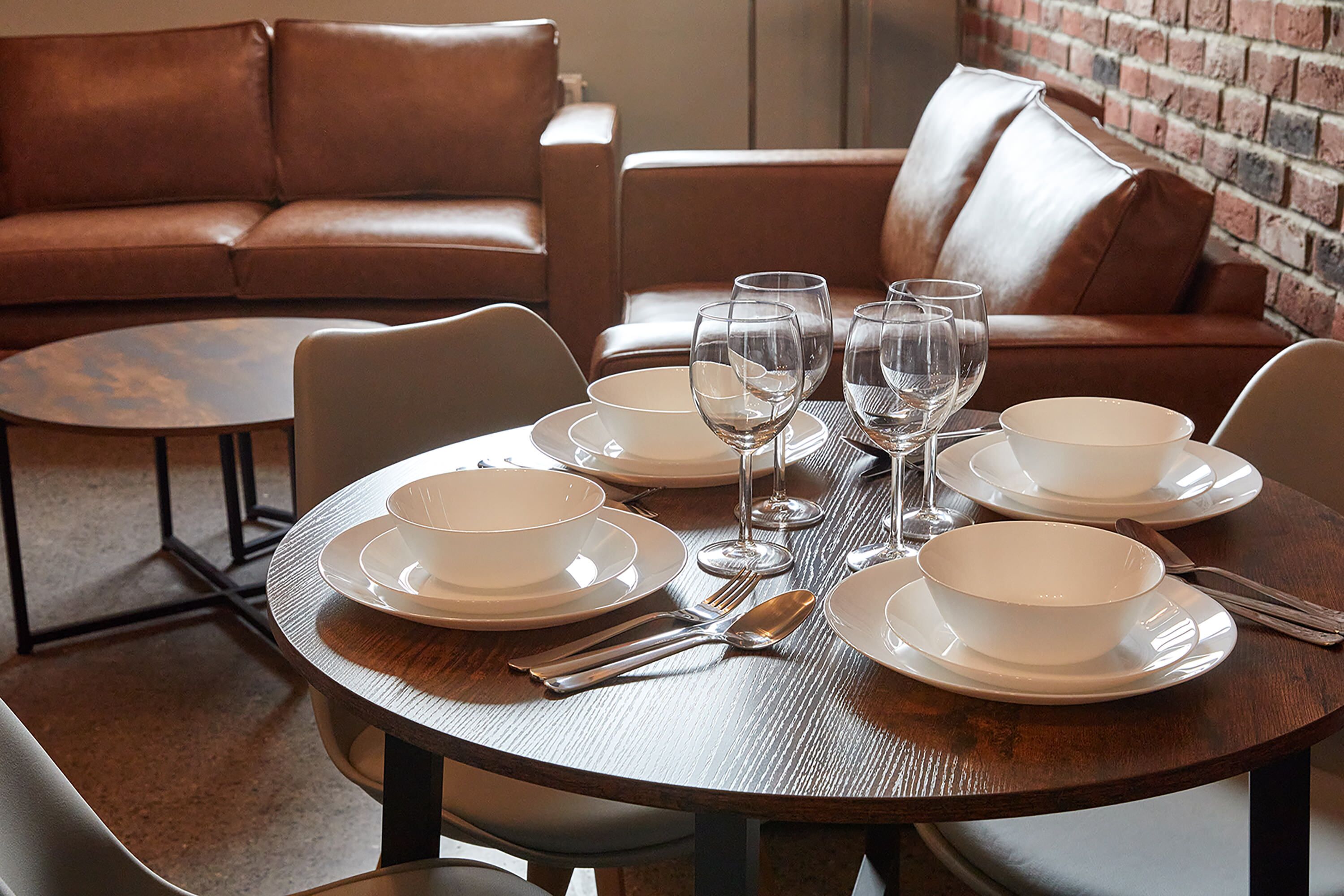A dining area with a round table set for four, surrounded by leather sofas.
