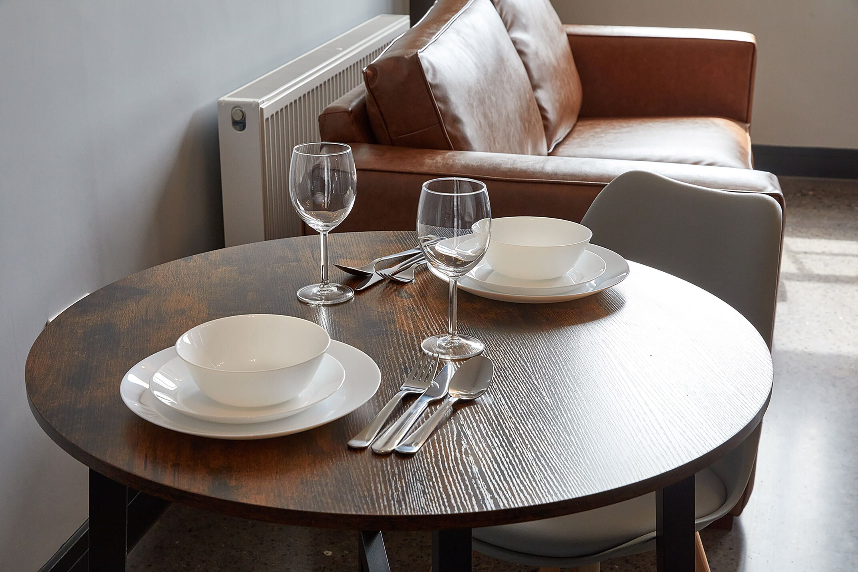 Een ronde eettafel met witte borden, kommen en bestek, gedekt voor twee personen.