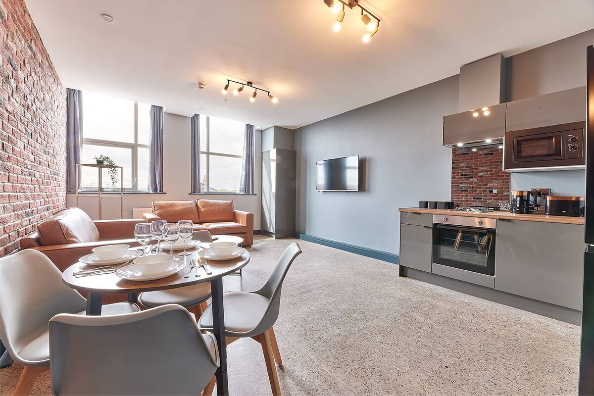 A modern kitchen with a built-in oven and microwave, a dining area with a table set for four, and a seating area with a sofa and chairs.