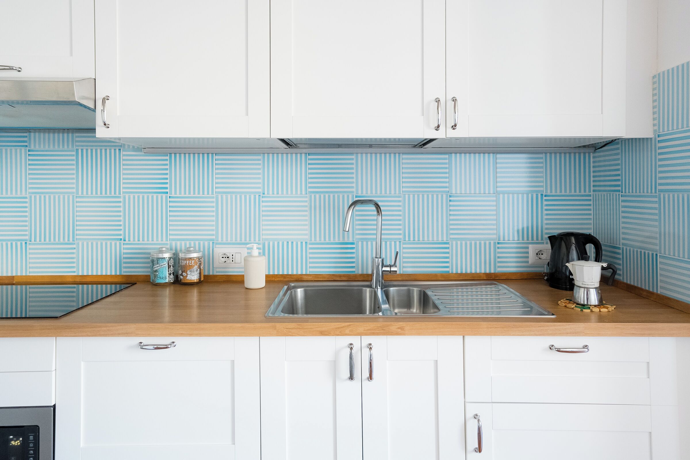 A modern kitchen with white cabinets, a stainless steel sink, and a coffee maker on the counter.