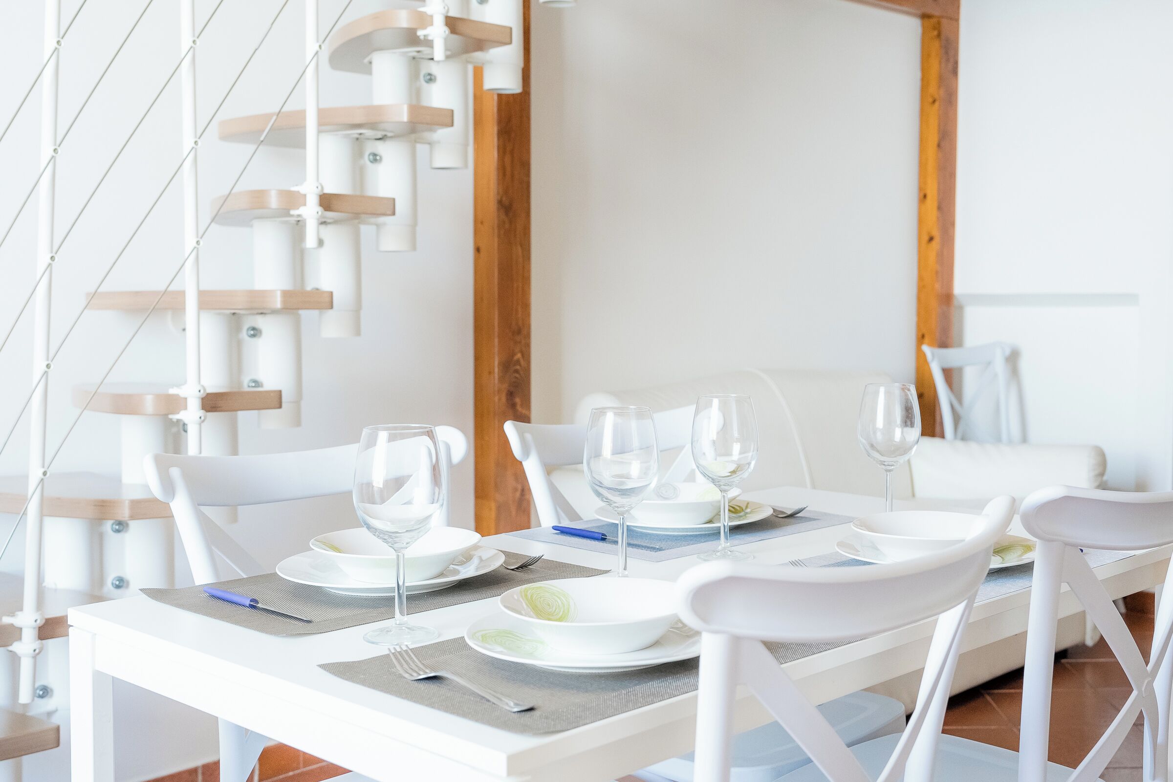 Una sala da pranzo con sedie bianche, un tavolo bianco e una scala in legno.