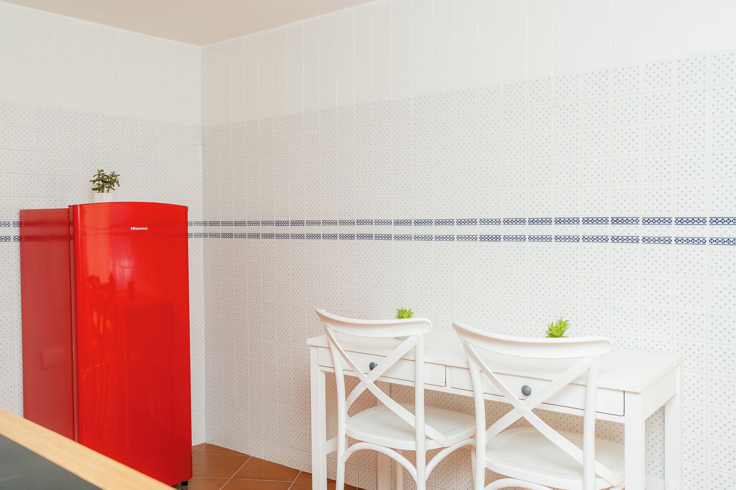 A compact kitchen with a red refrigerator, two white chairs, and a patterned backsplash.