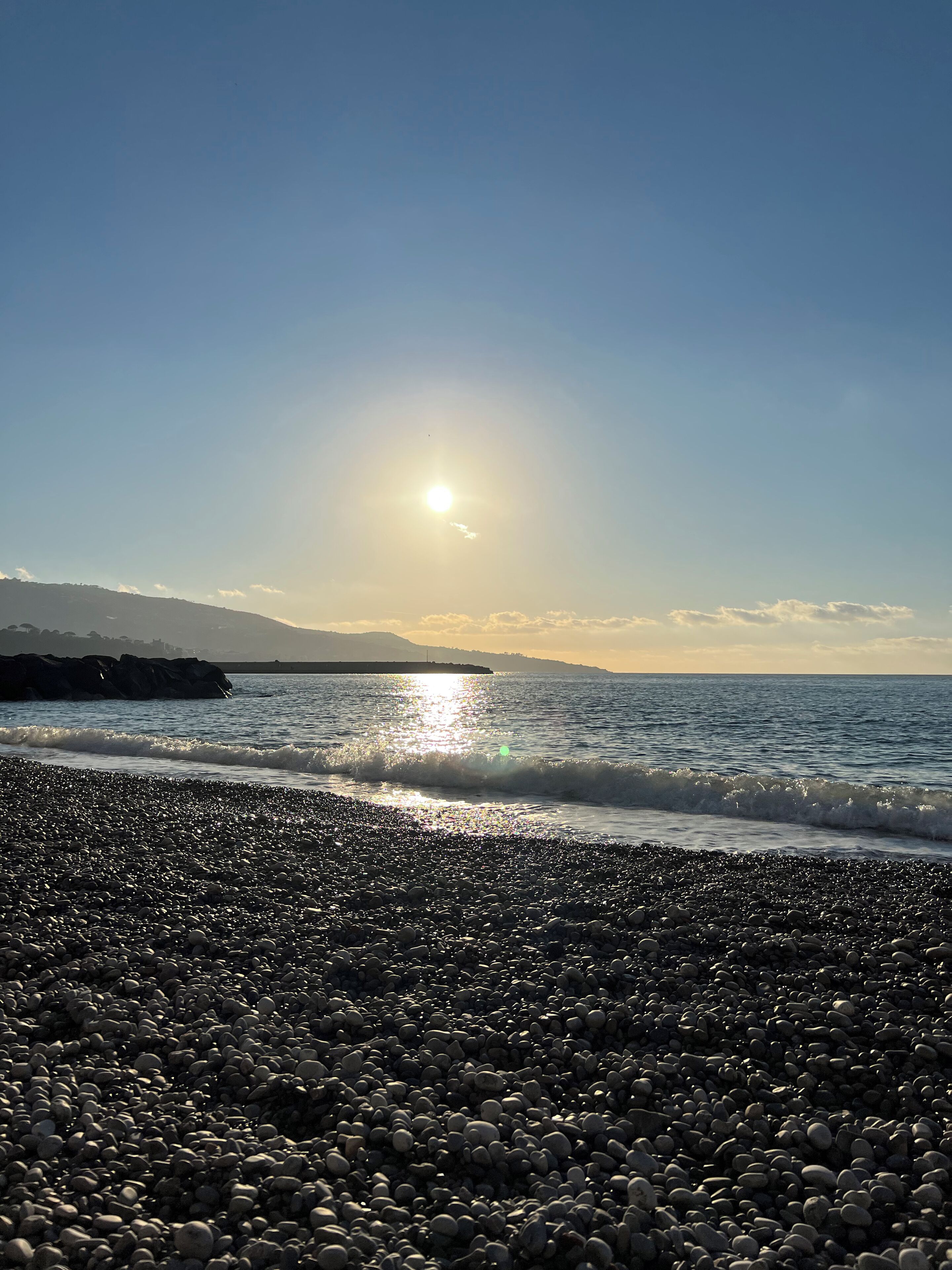 Una playa de guijarros con el sol reflejado en el agua.