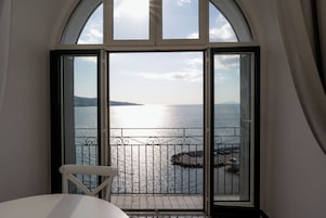 Una habitación con un gran ventanal con vistas a un cuerpo de agua, una barandilla de metal y una silla blanca.