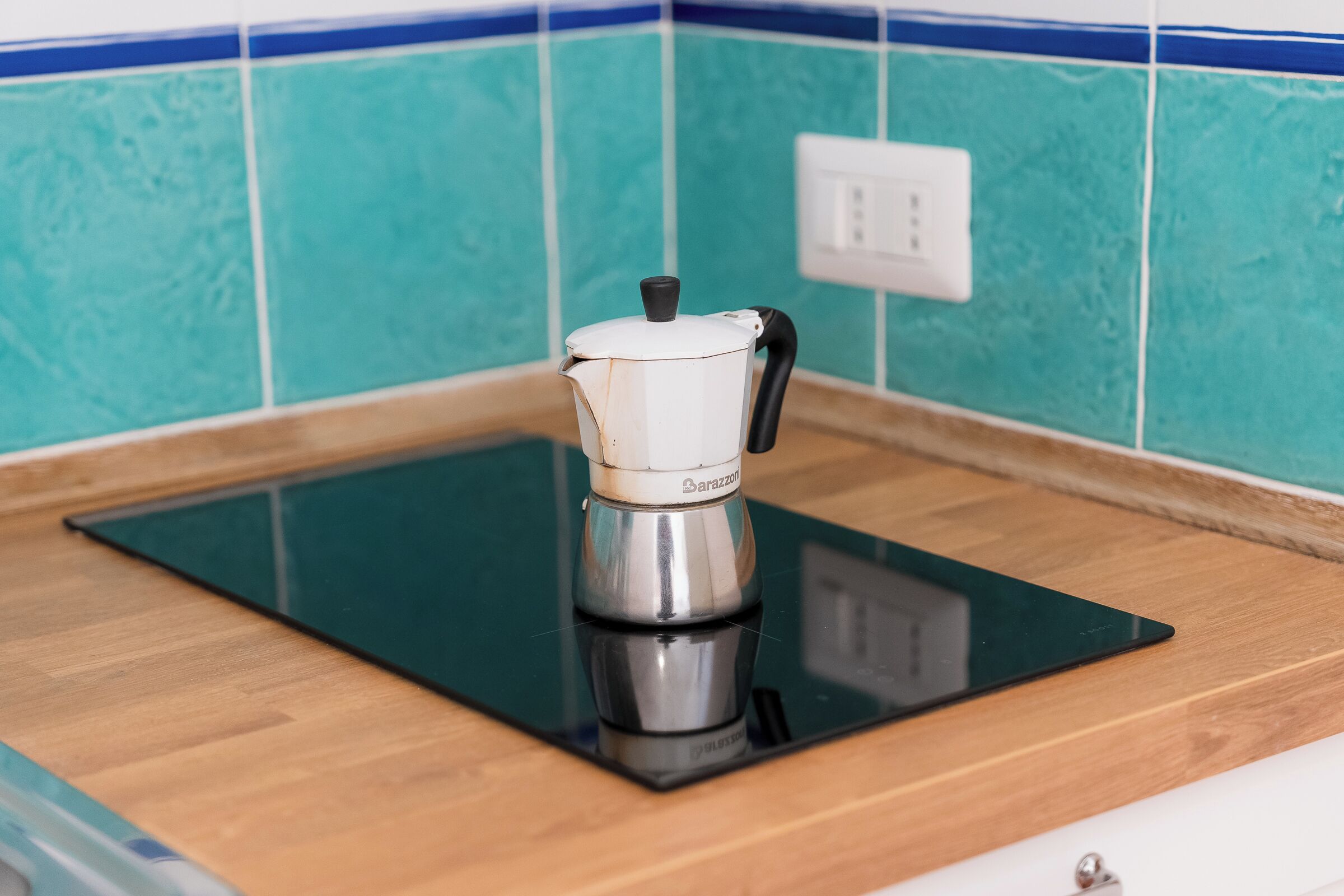A kitchen with a black countertop, a white coffee maker, and teal tiles.
