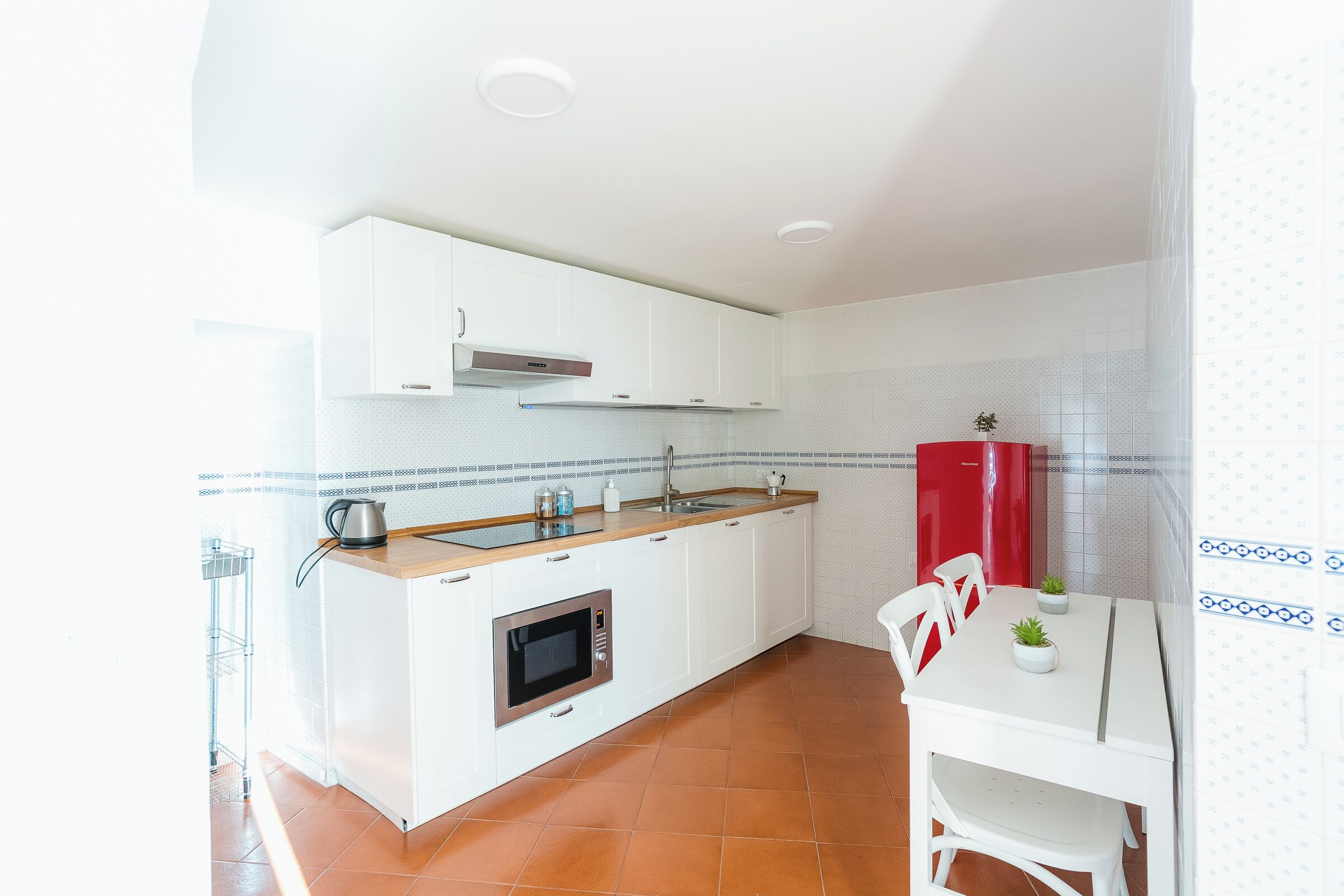 A compact kitchen with white cabinets, a red refrigerator, and a small dining table with chairs.