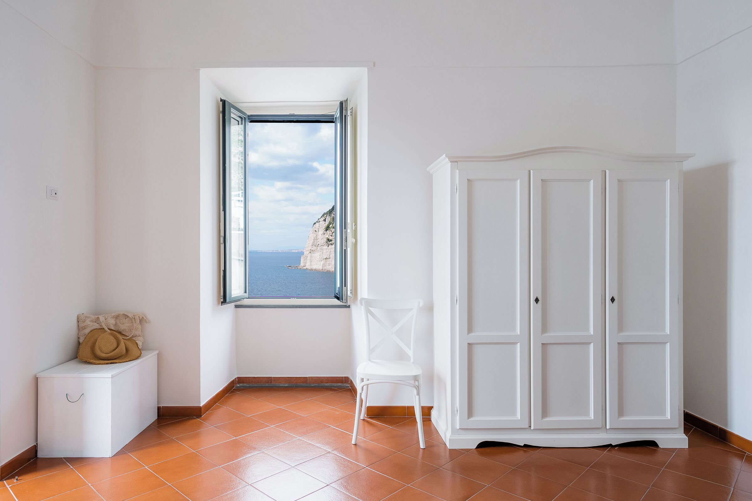 Ein Zimmer mit Meerblick, eine weiße Kommode und ein kleiner weißer Stuhl.