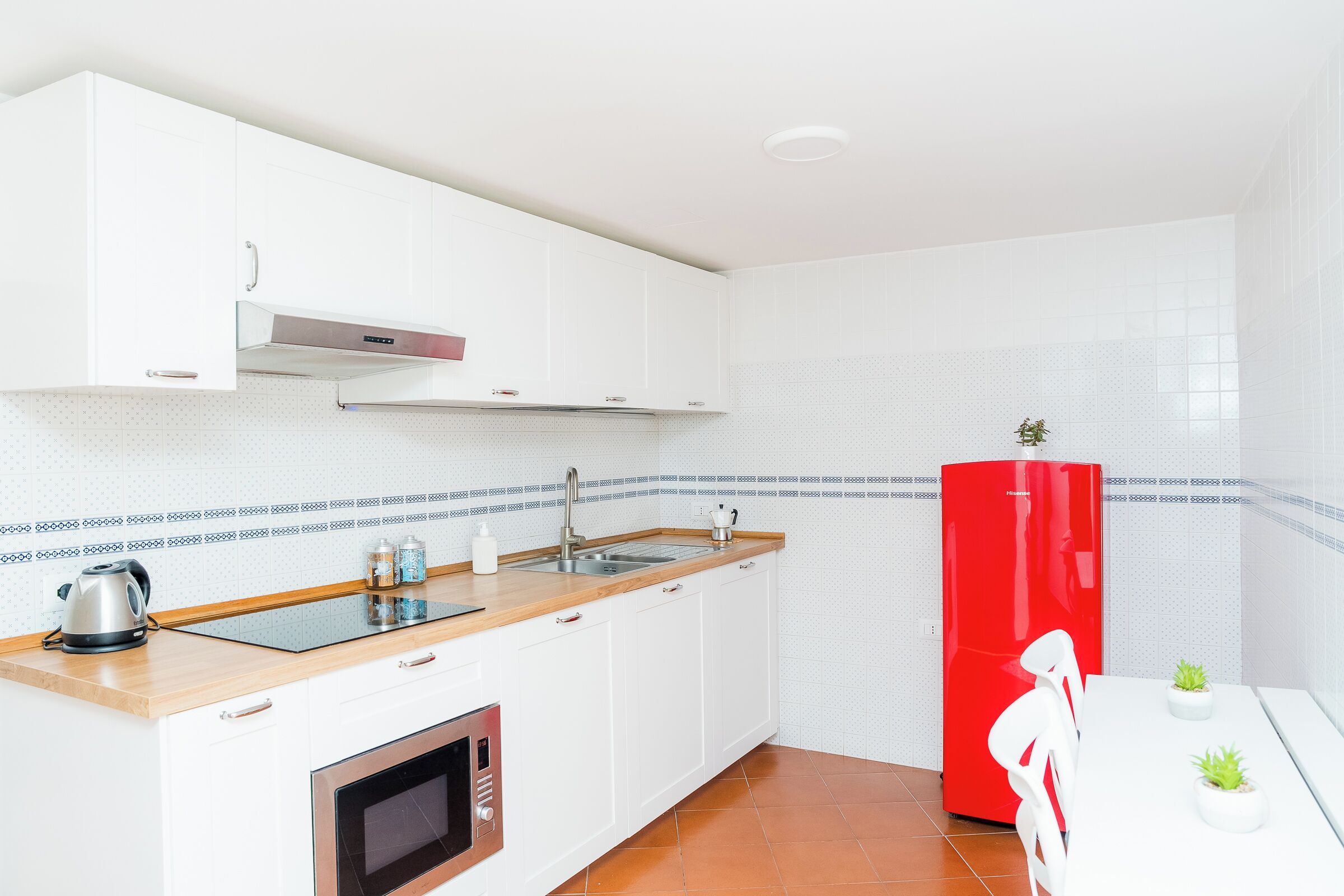 A modern kitchen with white cabinets, a red refrigerator, a sink, and a stove.