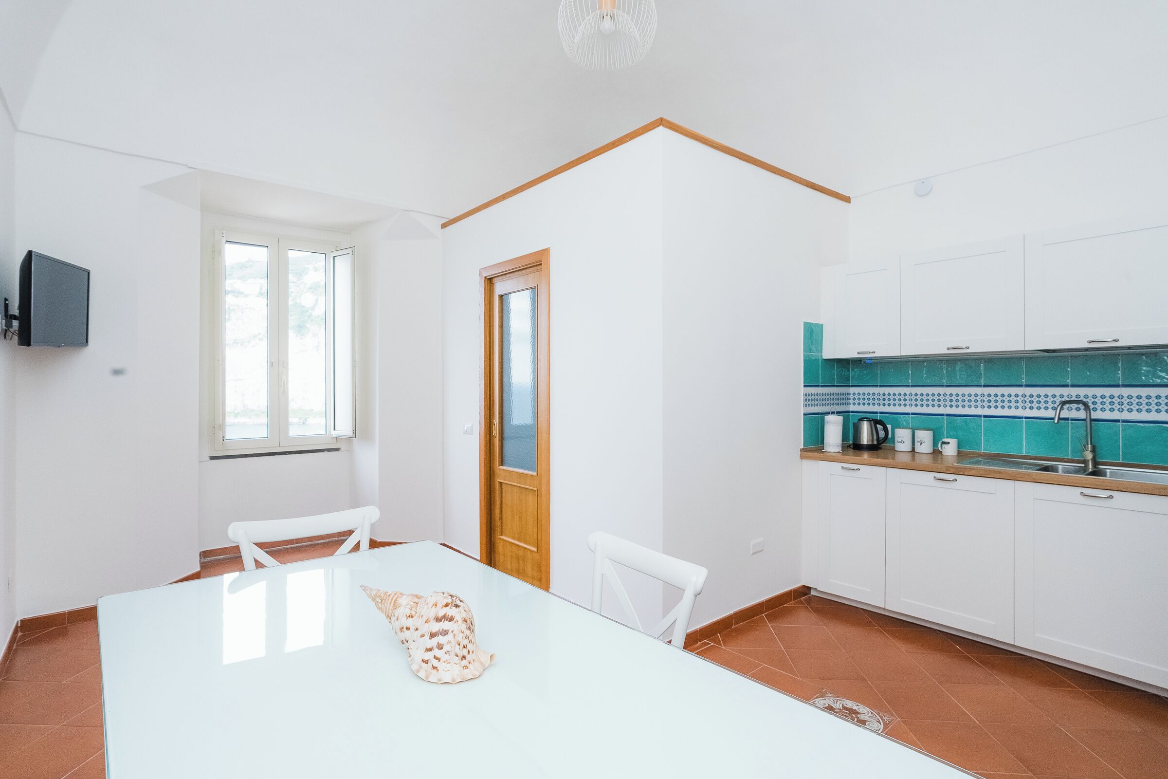 A modern kitchen with white cabinets, a tiled backsplash, and a dining area with a white table and chairs.