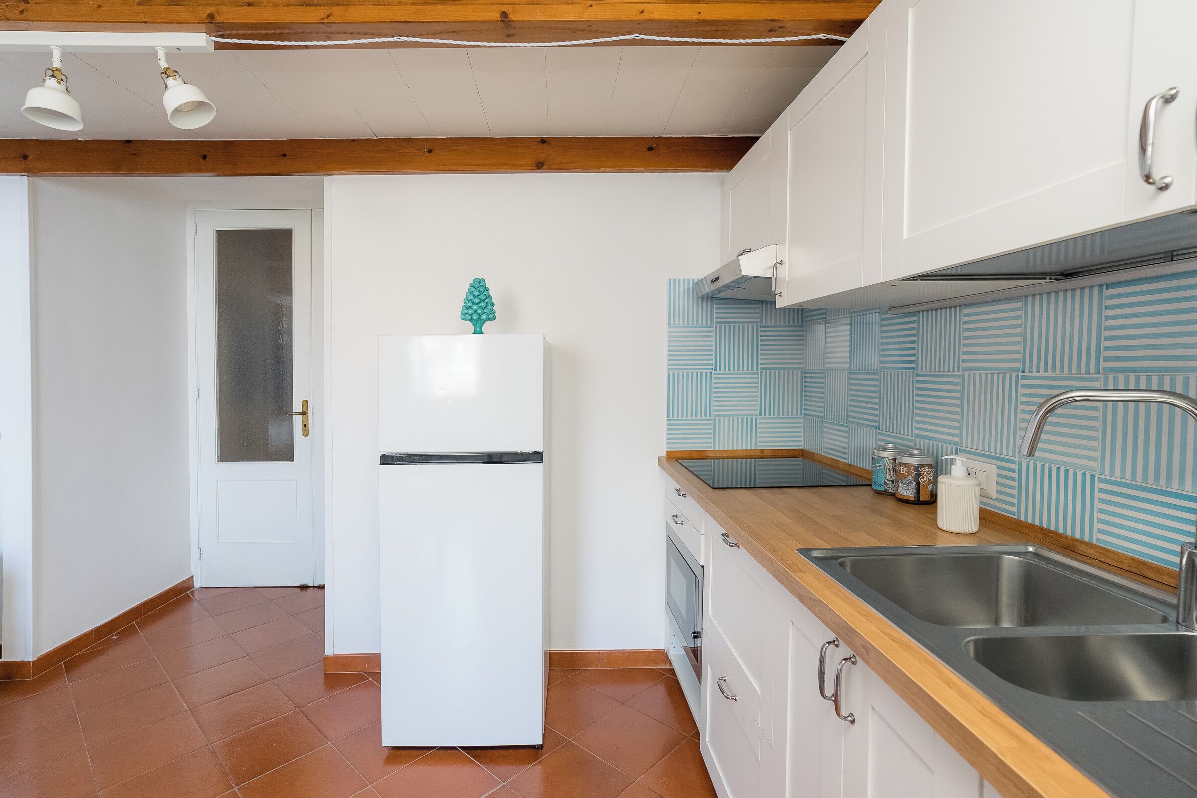 Una cocina con armarios blancos, encimera de madera y pileta de acero inoxidable.