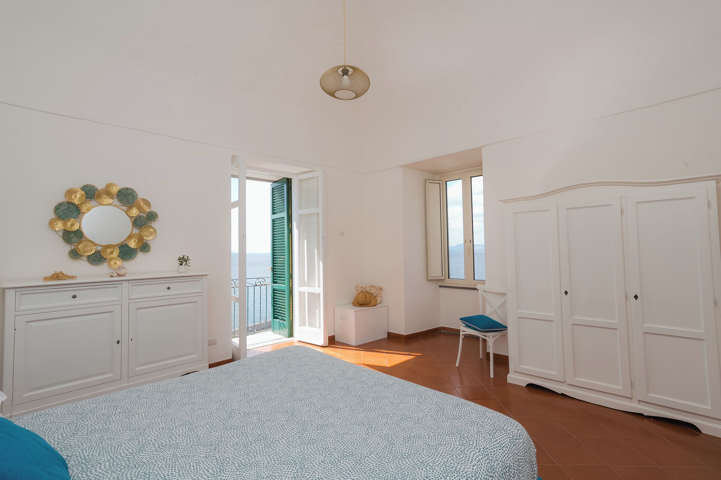 Un dormitorio con cama, armario, escritorio y vista al mar.