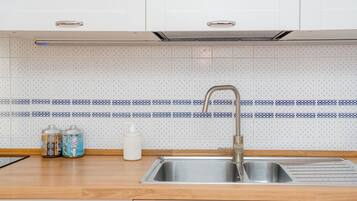 A kitchen with a stainless steel sink, wooden countertop, and patterned backsplash.