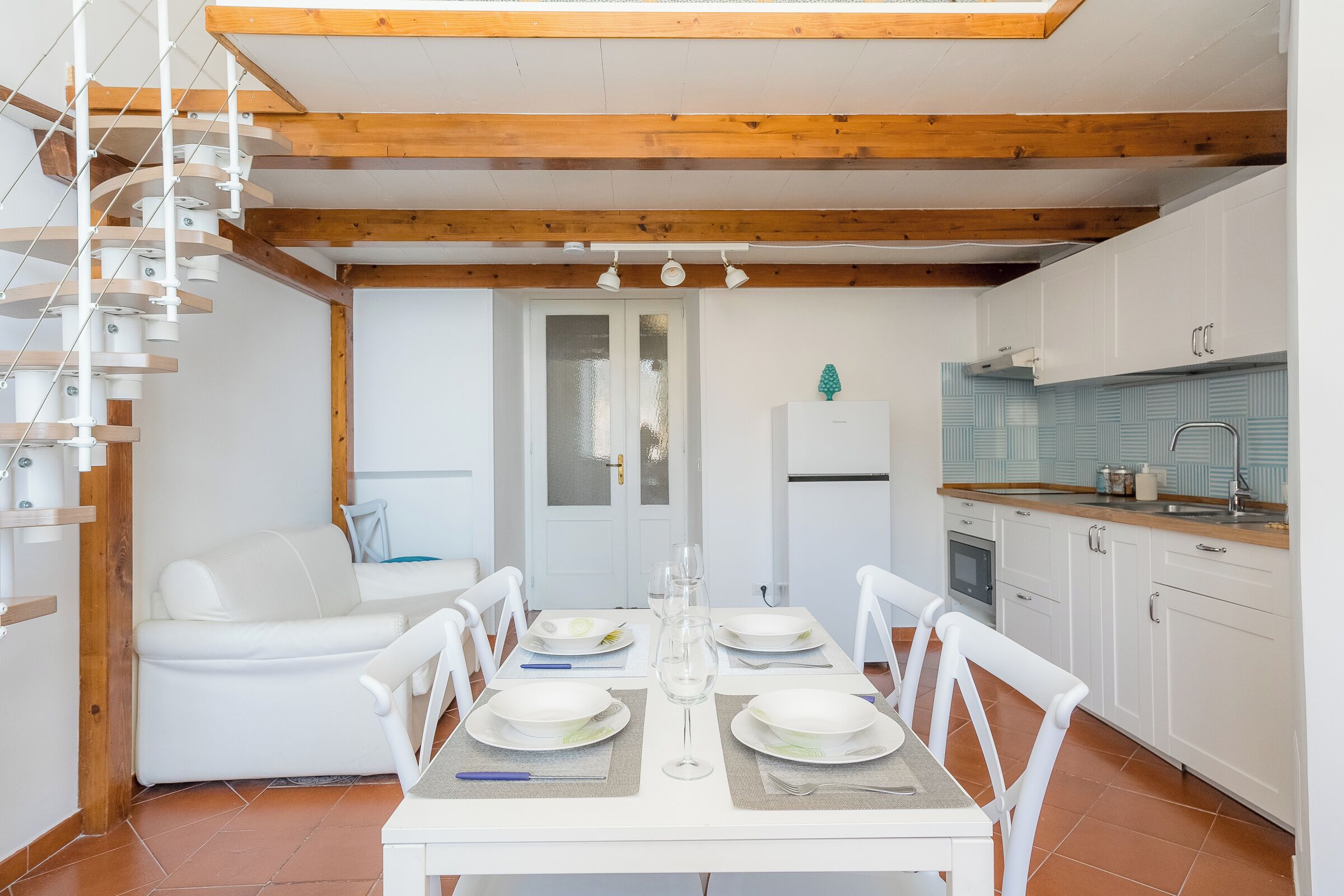 A modern kitchen with white cabinets, a wooden ceiling, and a dining area with a white table set for four.