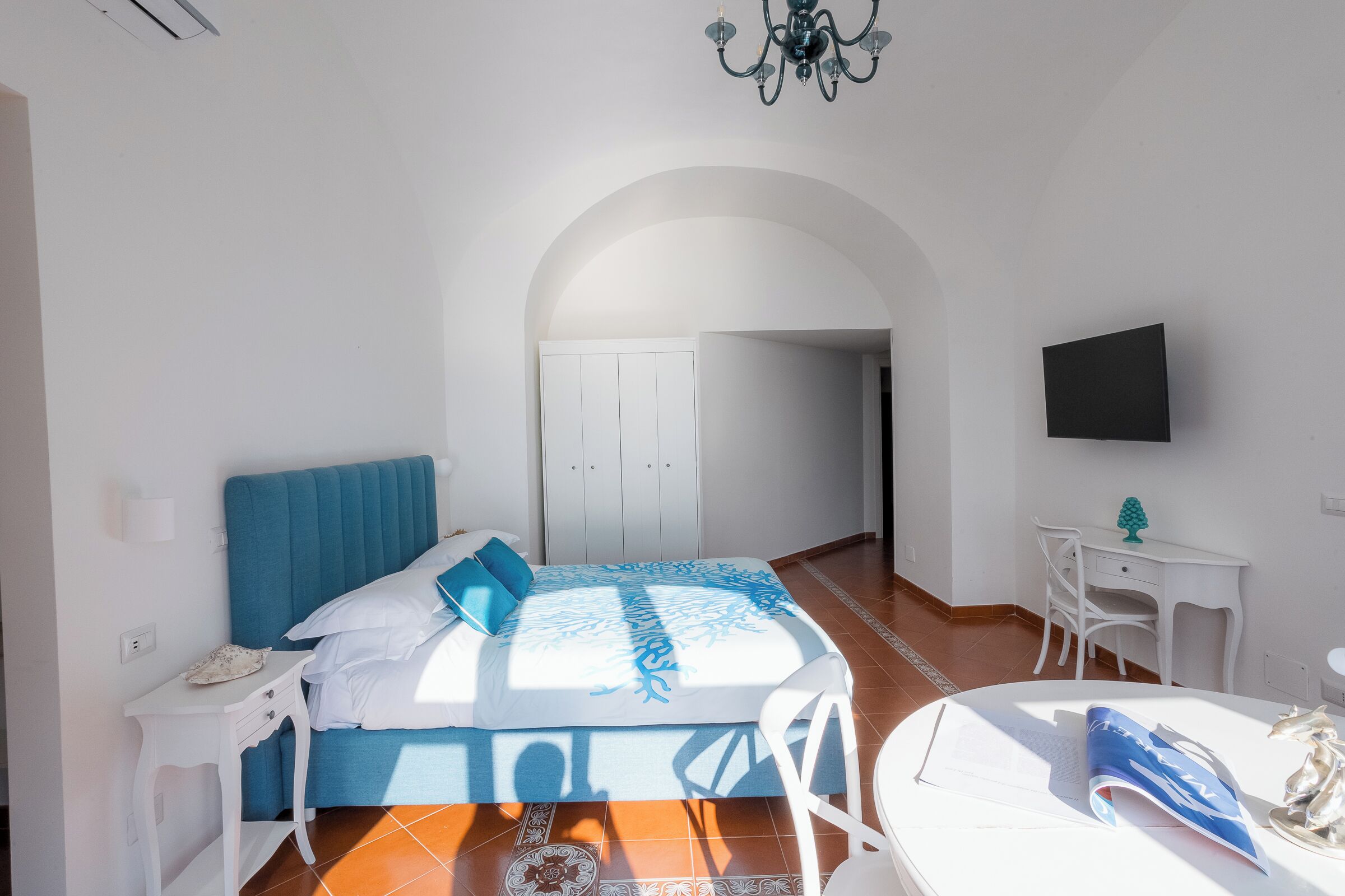 Un dormitorio con cama, escritorio, silla, televisor y un arco de entrada.