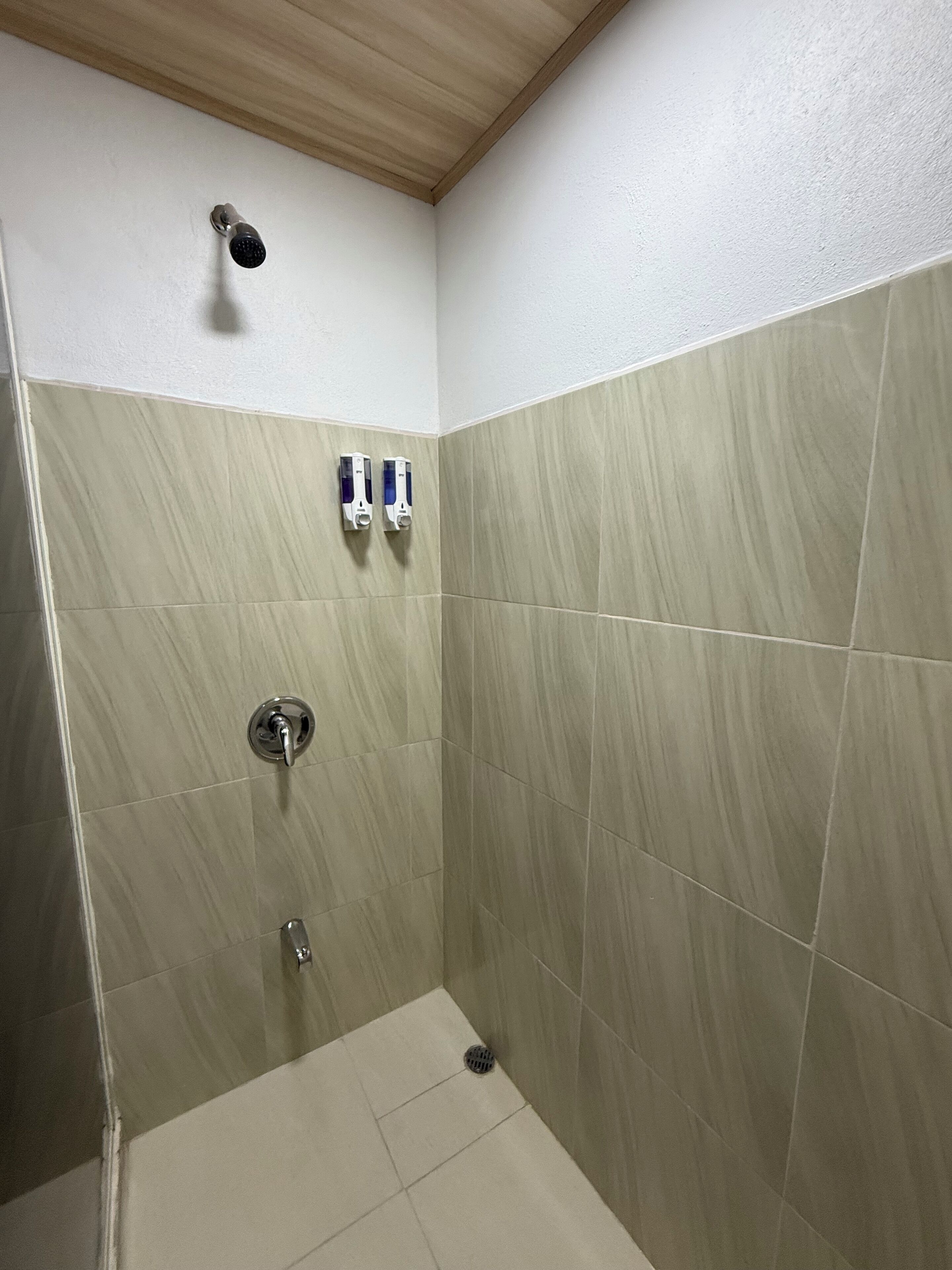 A small, tiled shower room with a wooden ceiling and two hand sanitizer dispensers mounted on the wall.
