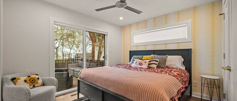 A bedroom with a bed, a chair, a ceiling fan, and a view through a sliding door to an outdoor area.