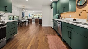 Una cocina moderna con armarios verdes, suelo de madera y un comedor con mesa y sillas.