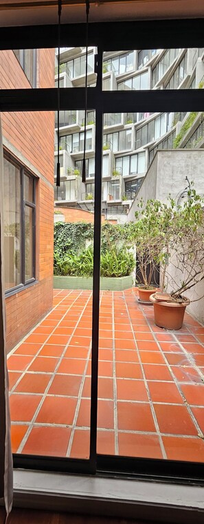 A view through a window of a courtyard with red-tiled flooring, potted plants, and a modern building with balconies and large windows. - Experience vibrant city living, steps away from all that Quito has to offer (Quito)