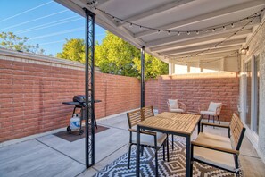 A covered patio with a brick wall, a grill, and outdoor furniture. - Charming Townhouse in Tucson. (Tucson)