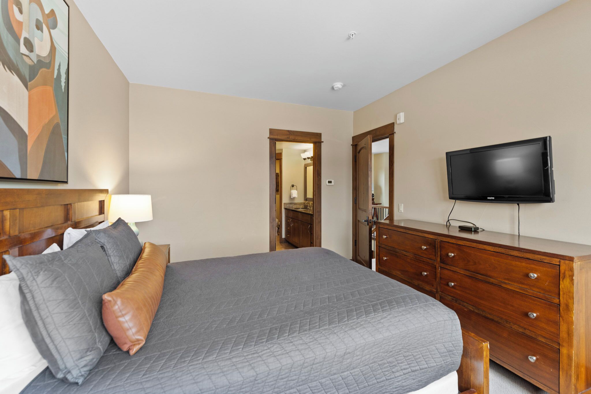 A hotel room with a bed, a dresser, a television, and a painting on the wall.