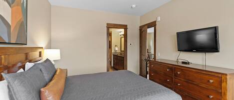 A hotel room with a bed, a dresser, a television, and a painting on the wall.