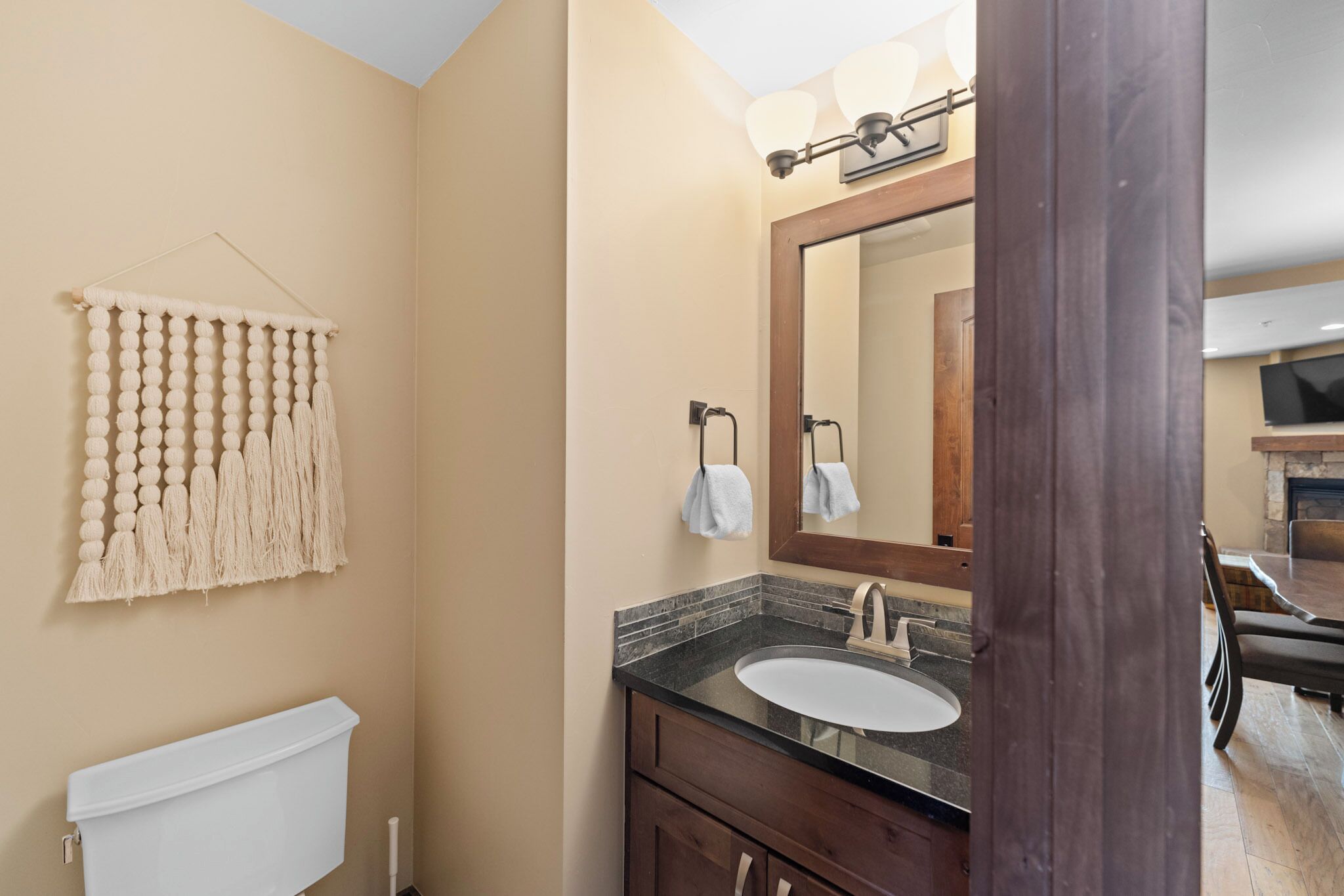 A bathroom with a beige wall, a white toilet, a sink with a dark countertop, and a mirror with a wooden frame.