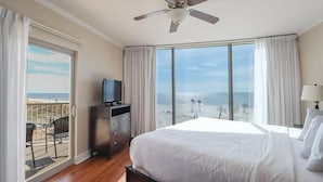 A hotel room with a bed, a TV on a dresser, a balcony with a chair, and a view of the beach. - Panoramic Gulf Views- Two bedroom condo-On the Beach with Balcony! (Biloxi)