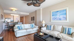 A modern living room with a white sofa set, a dining area, and a kitchen in the background. - Panoramic Gulf Views- Two bedroom condo-On the Beach with Balcony! (Biloxi)