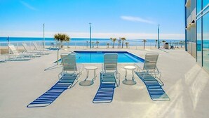 A pool area with lounge chairs and tables, a clear view of the beach, and a building with large windows. - Panoramic Gulf Views- Two bedroom condo-On the Beach with Balcony! (Biloxi)