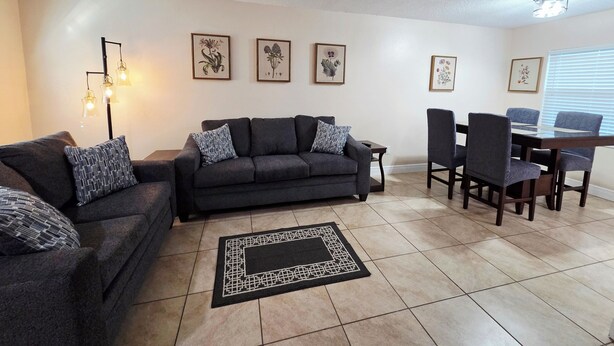 A living room with a dark grey sofa set, a dining table with chairs, and a patterned rug. - Toria Suites Condo 924 (Lakeland)