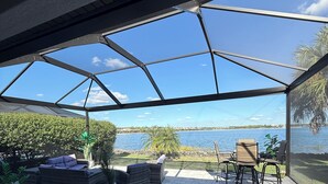 Eine überdachte Terrasse mit Gartenmöbeln und Blick auf das Wasser, bewölkter Himmel.