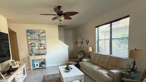Ein Wohnzimmer mit einem weißen Sofa, einem Couchtisch, einem Fernseher und einem Deckenventilator.