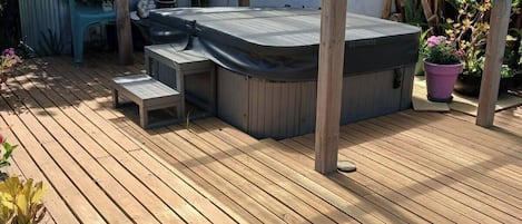 A wooden deck with a hot tub, a pergola, and potted plants.
