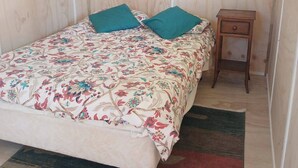 Ein kleiner Raum mit Holzwänden, einem Bett, zwei Kissen, einem Nachttisch und einem Teppich.
