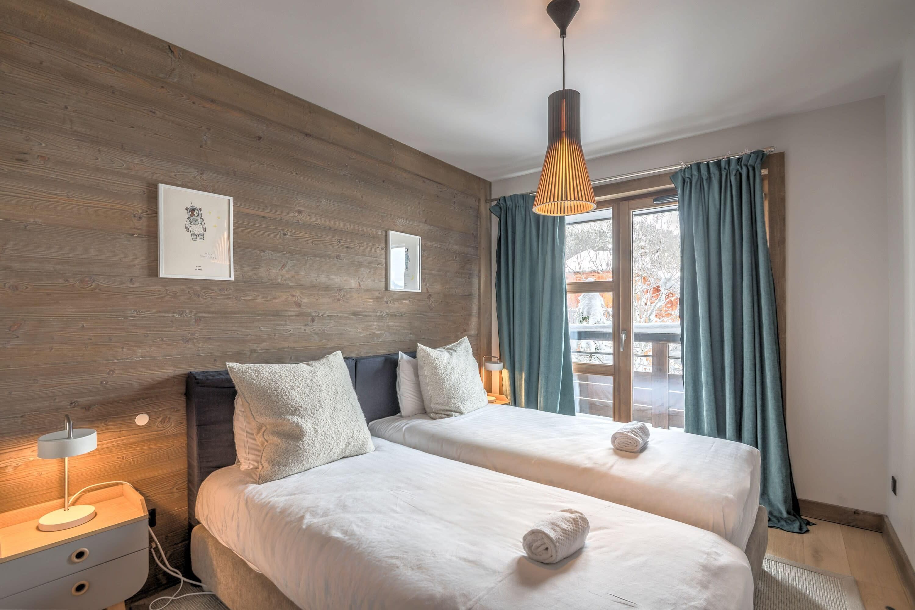 Ein Hotelzimmer mit zwei Betten, einer Holzwand, einem Fenster mit Vorhängen und einer Pendelleuchte.