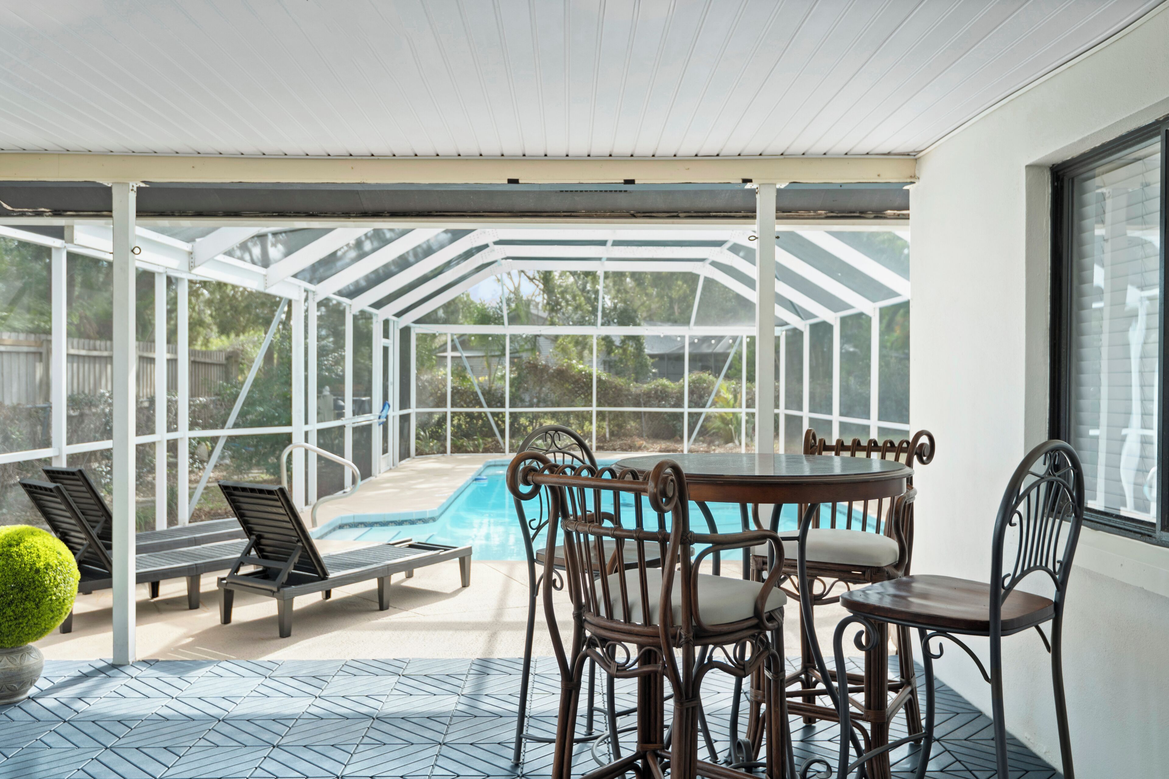 A covered outdoor area with a pool, lounge chairs, and a table with chairs.