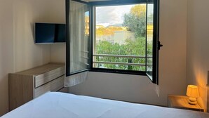 Une chambre d’hôtel avec un lit, un téléviseur fixé au mur, une fenêtre avec un rideau ouvert et une table de chevet avec une lampe.