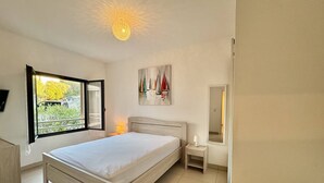 Une chambre à coucher avec un lit, une table de chevet, une lampe, un tableau, une fenêtre donnant sur un beau paysage et une chaise.