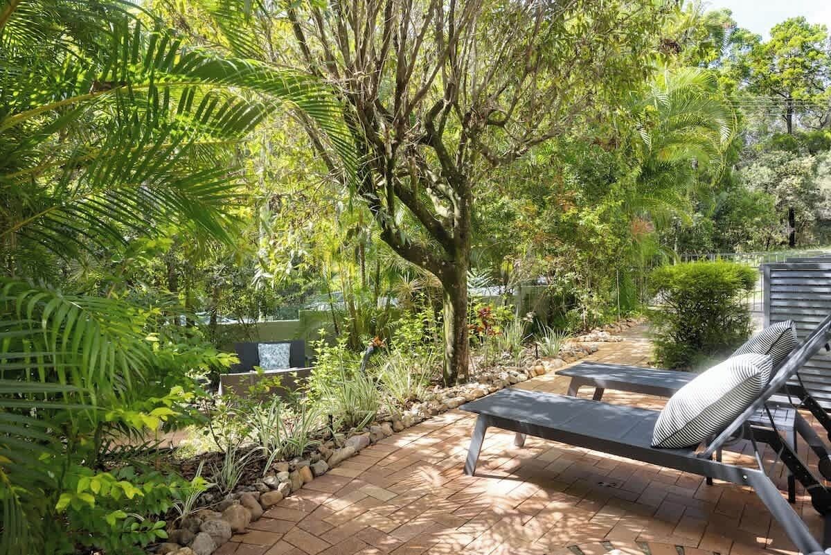 Un patio giardino con una poltrona da relax e un tavolino, immerso nel verde e alberato.