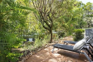 Eine Garten-Terrasse mit Liegestuhl und kleinem Tisch, umgeben von üppiger Bepflanzung und einem Baum.