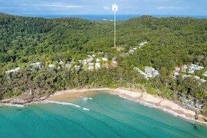 Eine Küstenlandschaft mit Strand, dichtem Wald und einem weißen Gebäude auf einem Hügel.