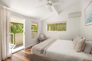Ein Schlafzimmer mit einem Bett, einem Sessel, einem Deckenventilator und einem Fenster mit Blick auf Grünflächen.