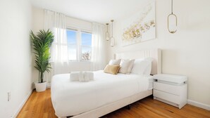 Un dormitorio moderno con una cama grande, mesitas de noche, una planta en maceta y vistas al exterior.