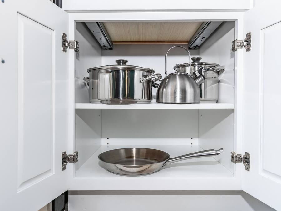 Ein Küchenschrank mit Edelstahlkochgeschirr, darunter Töpfe, ein Wasserkocher und eine Bratpfanne.