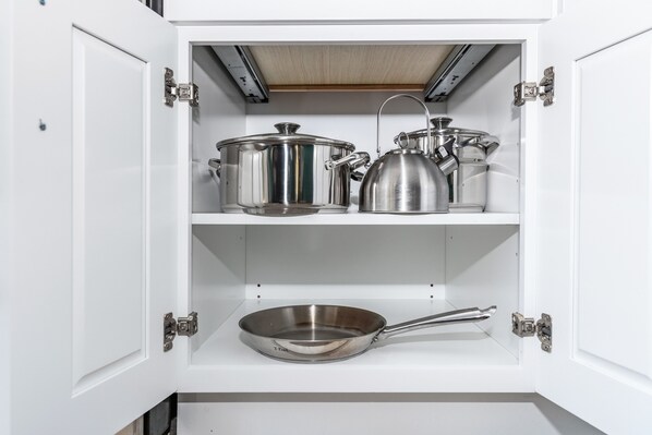 Un mueble de cocina con utensilios de acero inoxidable, incluyendo ollas, un hervidor y una sartén.