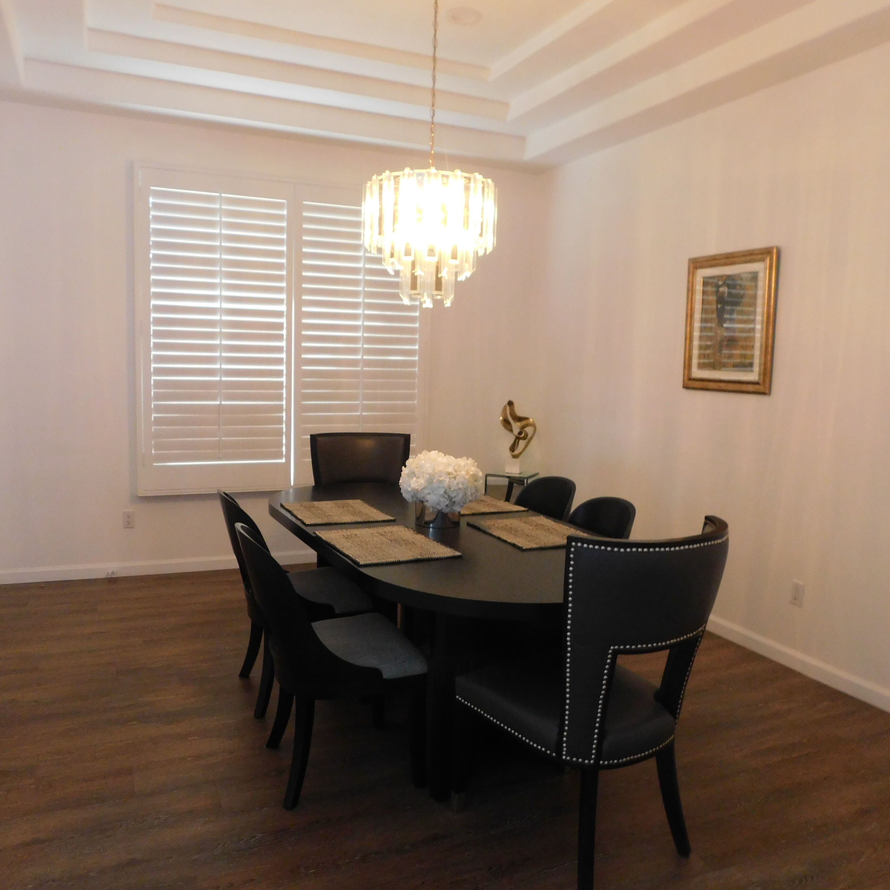Ein Esszimmer mit rundem Tisch, schwarzen Stühlen, einer Pendelleuchte und einem gerahmten Bild an der Wand.
